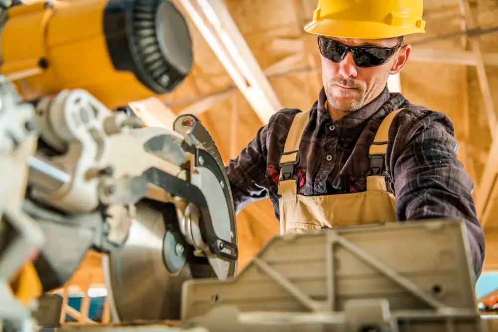 Worker cutting a beam of wood with a table saw and who know the reasons why general contractors need general liability insurance