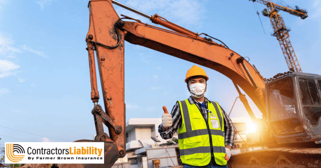 Construction worker wearing a hard hat and reflective safety vest gives a thumbs-up beside an excavator at a construction site.